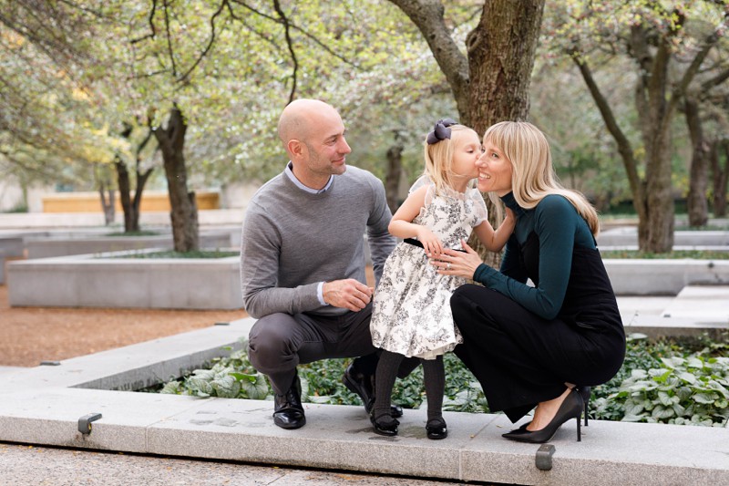 a little girl kisses her mom on the cheek while her dad watches on at the south garden at the chicago art institute
