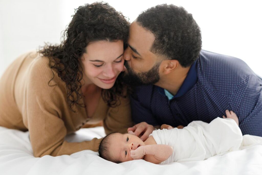 newborn-photography-ideas-dad kissing mom while looking at baby