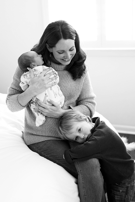 mom holding her newborn baby with son hugging her legs