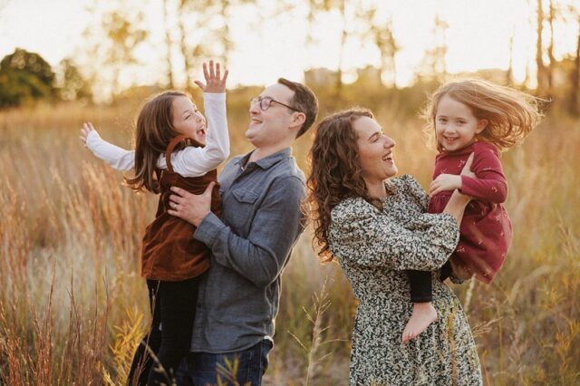 a mother and father play with their two daughters in a field at montrose harbor in chicago