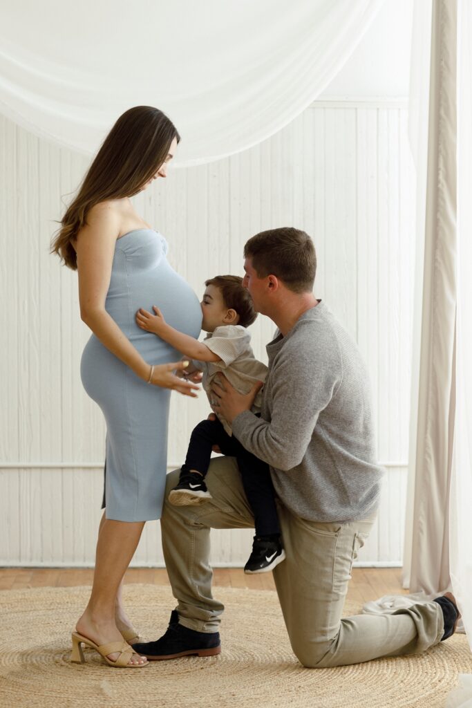 a little boy kisses his moms pregnant belly during her maternity photoshoot