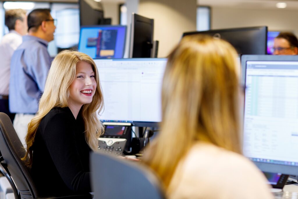 two women financial traders talk together at their desks