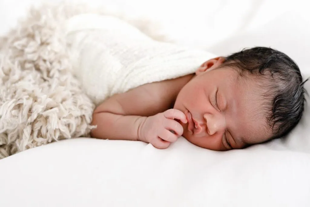 newborn baby laying on a white bed wrapped in layered swaddles