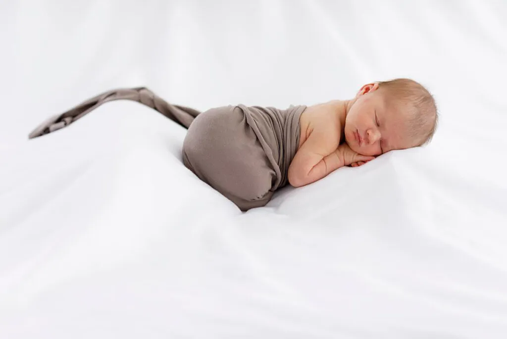 newborn baby swaddled on a white bed