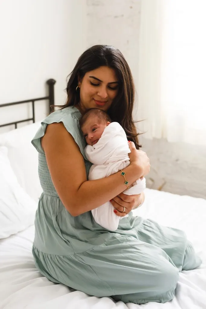 mom wearing a green, gauzy dress holding her baby in her arms during a newborn photoshoot
