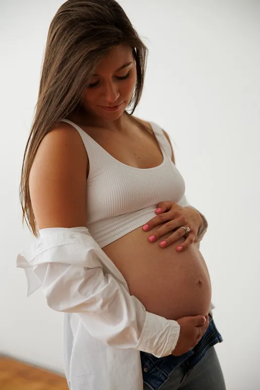 a pregnant woman in profile poses holding her belly in a white shirt, white top